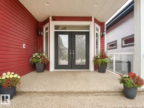 Double entry doors with patterned glass, exposed aggregate concrete porch, red horizontal siding, and white trim accents - 27 Kingdom Place, Leduc, AB - Outdoor With Exterior