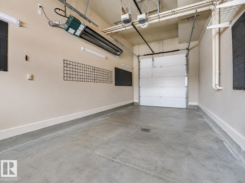 Concrete flooring with a white rolling garage door - 27 Kingdom Place, Leduc, AB - Indoor Photo Showing Garage