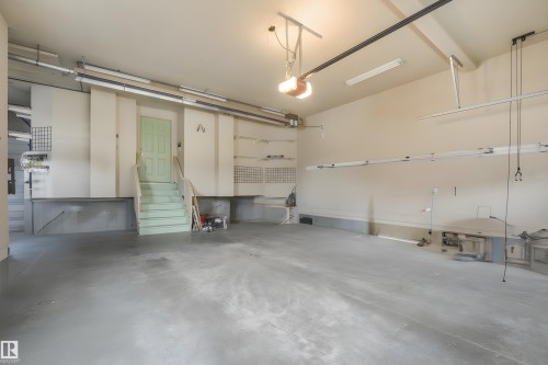 Spacious garage featuring a light green interior door, built-in shelving, and overhead lighting - 27 Kingdom Place, Leduc, AB - Indoor Photo Showing Garage