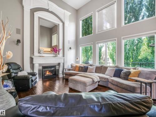 Two-story living area featuring a fireplace with ornate mantel, dark wood-finish flooring, and multiple large windows - 967 Lamb Crescent Nw, Edmonton, AB - Indoor Photo Showing Living Room With Fireplace