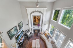 Vaulted ceiling with a ceiling fan, a fireplace with an ornate white mantel, rich wood-finish flooring, and multiple large windows - 