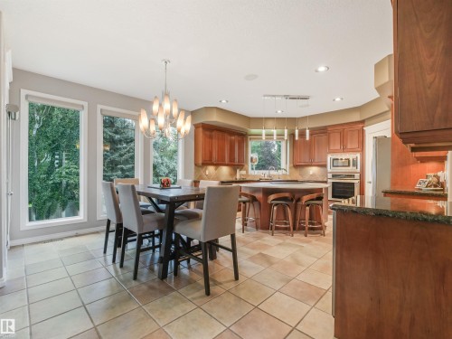 Spacious kitchen featuring warm wood cabinetry, a large center island with seating, integrated wall oven and microwave, stone countertops, and tile flooring - 967 Lamb Crescent Nw, Edmonton, AB - Indoor Photo Showing Other Room