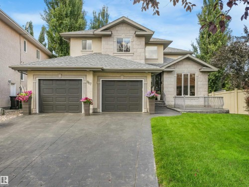 Stucco exterior with stone accents, dual garage doors, stamped concrete driveway, mature landscaping, and a fenced perimeter - 967 Lamb Crescent Nw, Edmonton, AB - Outdoor With Facade