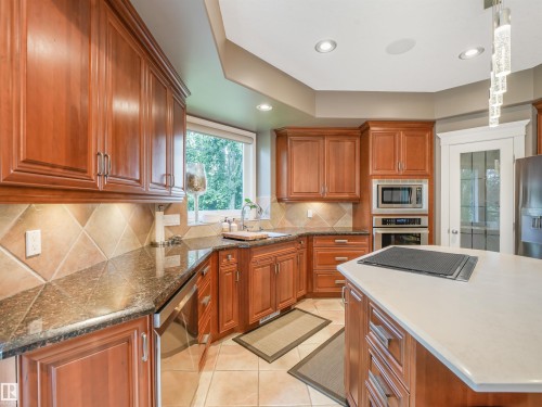 Kitchen featuring wood cabinetry, integrated stainless steel appliances, a center island with light-toned countertop, dark-toned perimeter countertops, and a tiled backsplash - 967 Lamb Crescent Nw, Edmonton, AB - Indoor Photo Showing Kitchen