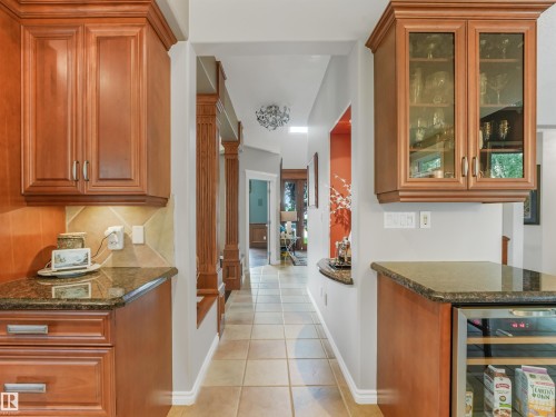 Wood-finish cabinetry with glass-front uppers, polished stone countertops, tile flooring, and a built-in beverage cooler - 967 Lamb Crescent Nw, Edmonton, AB - Indoor Photo Showing Kitchen