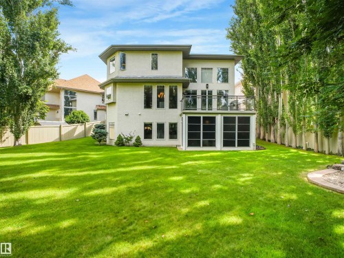 Expansive green lawn, stucco exterior, upper-level balcony with glass railing, ground-level screened-in area, and mature perimeter trees - 967 Lamb Crescent Nw, Edmonton, AB - Outdoor