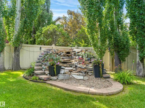 Landscaped backyard featuring a stone water feature, mature trees, manicured lawn, and a privacy fence - 967 Lamb Crescent Nw, Edmonton, AB - Outdoor
