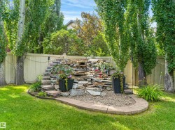 Landscaped backyard featuring a stone water feature, mature trees, manicured lawn, and a privacy fence - 