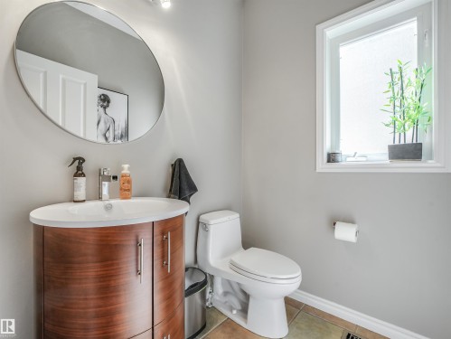 Powder room featuring a wood-finish vanity with an integrated sink, a contemporary round mirror, and a window with privacy glass - 967 Lamb Crescent Nw, Edmonton, AB - Indoor Photo Showing Bathroom