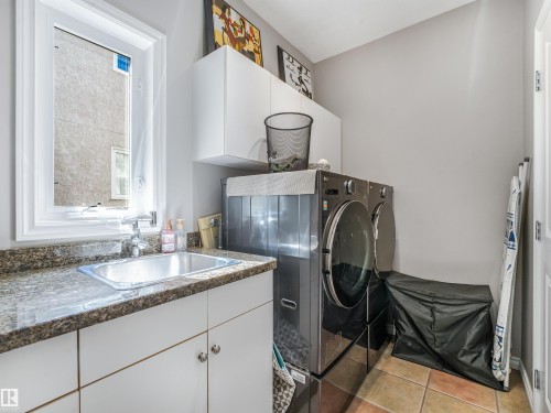 Laundry area with a window, built-in sink, stone-finish countertop, white cabinetry, and tile flooring - 967 Lamb Crescent Nw, Edmonton, AB - Indoor Photo Showing Laundry Room