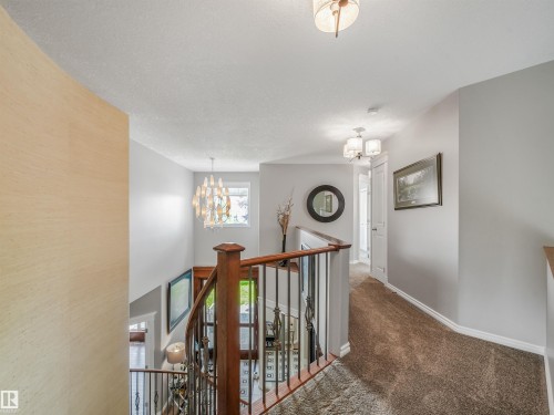 Upper-level landing with carpet flooring, wood handrail with metal spindles, and a multi-arm chandelier - 967 Lamb Crescent Nw, Edmonton, AB - Indoor Photo Showing Other Room