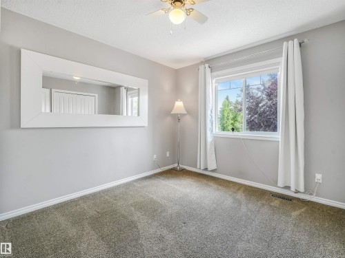 Wall-mounted rectangular mirror, ceiling fan with integrated lighting, window with exterior scenery, light gray wall color, and carpeted flooring - 967 Lamb Crescent Nw, Edmonton, AB - Indoor Photo Showing Other Room