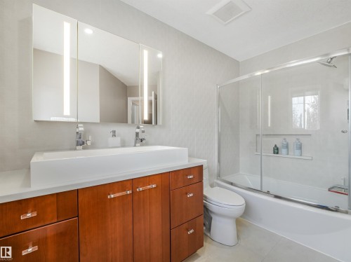 Double vanity with rectangular vessel sinks, illuminated medicine cabinets, and a bathtub with a sliding glass enclosure - 967 Lamb Crescent Nw, Edmonton, AB - Indoor Photo Showing Bathroom