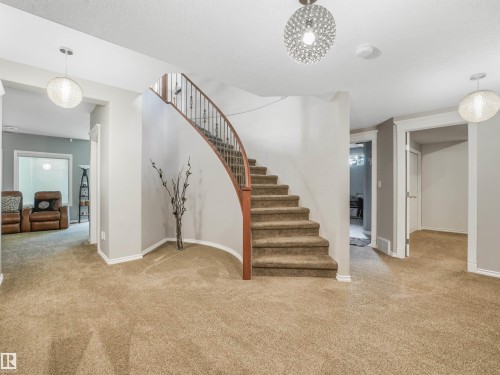 Curved staircase with wood railing, carpeted flooring, and modern ceiling light fixtures - 967 Lamb Crescent Nw, Edmonton, AB - Indoor Photo Showing Other Room