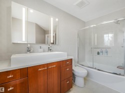 Double vanity with rectangular vessel sinks, illuminated medicine cabinets, and a bathtub with a sliding glass enclosure - 