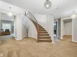 Curved staircase with wood railing, carpeted flooring, and modern ceiling light fixtures - 