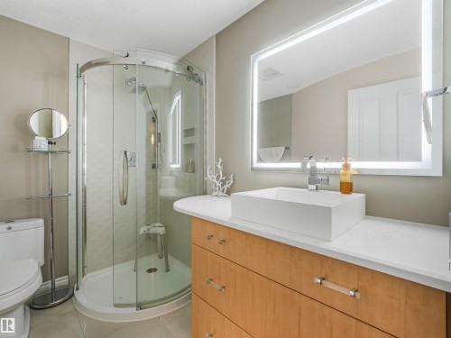 Curved glass shower enclosure, wood-finish vanity with ample storage, rectangular vessel sink, polished chrome faucet, and backlit vanity mirror - 967 Lamb Crescent Nw, Edmonton, AB - Indoor Photo Showing Bathroom