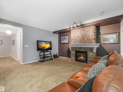 Stone-faced fireplace with a white mantel, recessed electric insert, track lighting, and wall-to-wall carpeting - 967 Lamb Crescent Nw, Edmonton, AB - Indoor Photo Showing Living Room With Fireplace