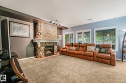 Stone-clad fireplace with a white mantel, recessed lighting, track lighting, light-toned carpeting, and multiple windows - 