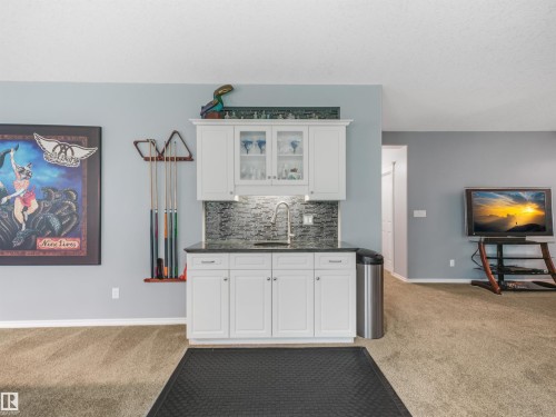 Built-in wet bar with white cabinetry, dark countertop, and tile backsplash - 967 Lamb Crescent Nw, Edmonton, AB - Indoor