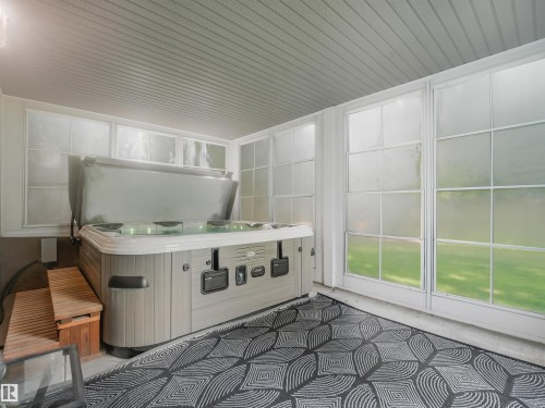 Covered outdoor area featuring a hot tub, large picture windows, wood steps, and a patterned area rug - 967 Lamb Crescent Nw, Edmonton, AB - Indoor Photo Showing Other Room