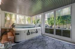 Screened-in porch featuring a built-in hot tub, wood steps, and multiple large windows - 