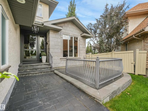 Stone facade with a double glass entry door, an adjacent elevated patio featuring a decorative metal railing, a stamped concrete pathway, and a privacy fence - 967 Lamb Crescent Nw, Edmonton, AB - Outdoor