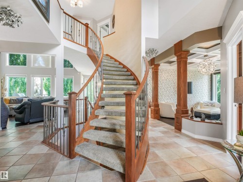 Grand two-story foyer featuring a curved staircase with wood and wrought iron balusters, diamond-patterned tile flooring, recessed coffered ceilings, and decorative columns - 967 Lamb Crescent Nw, Edmonton, AB - Indoor Photo Showing Other Room