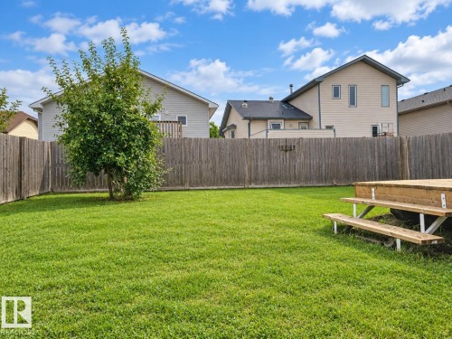 Expansive grassy yard with a mature tree, wooden privacy fencing, and a built-in wooden deck with steps - 507 Wiseman Lane Nw, Edmonton, AB 