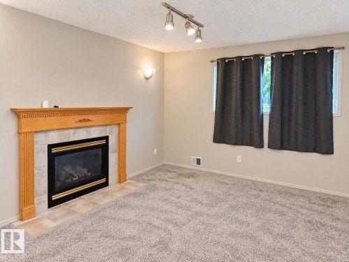 Fireplace featuring a wood mantel with decorative trim, tile surround, and a tile hearth - 507 Wiseman Lane Nw, Edmonton, AB 