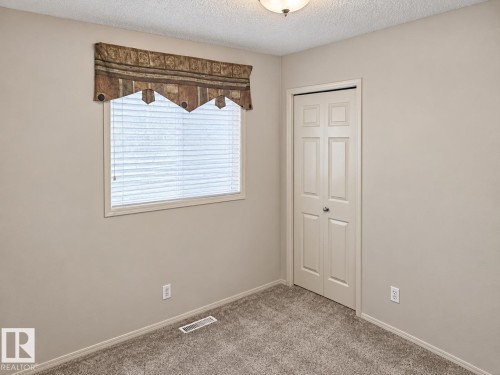 Neutral wall paint, textured ceiling, window with blinds, bi-fold closet door, and carpet flooring - 507 Wiseman Lane Nw, Edmonton, AB 