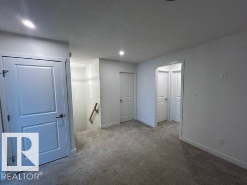 Plush grey carpeting, white interior doors with dark hardware, recessed ceiling lighting, and a staircase with a wood handrail - 20936 16 Avenue Nw, Edmonton, AB - Indoor Photo Showing Other Room