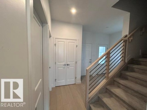 Light wood-finish flooring, white double-panel doors, recessed lighting, carpeted staircase, and a wood railing with black metal spindles - 20936 16 Avenue Nw, Edmonton, AB - Indoor Photo Showing Other Room