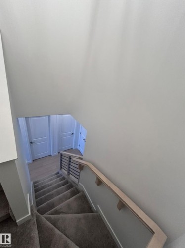 Carpeted staircase with light wood-finish handrail, horizontal metal balusters, and white interior doors - 20936 16 Avenue Nw, Edmonton, AB - Indoor Photo Showing Other Room