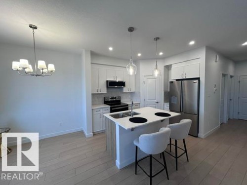 Modern kitchen featuring stainless steel appliances, white cabinetry, a central island with seating, and pendant lighting - 20936 16 Avenue Nw, Edmonton, AB - Indoor