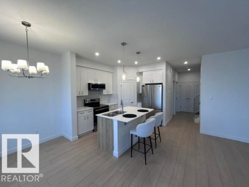 Modern kitchen featuring stainless steel appliances, white cabinetry, a center island with pendant lighting, recessed lighting, and wood-finish flooring - 20936 16 Avenue Nw, Edmonton, AB - Indoor Photo Showing Kitchen With Double Sink