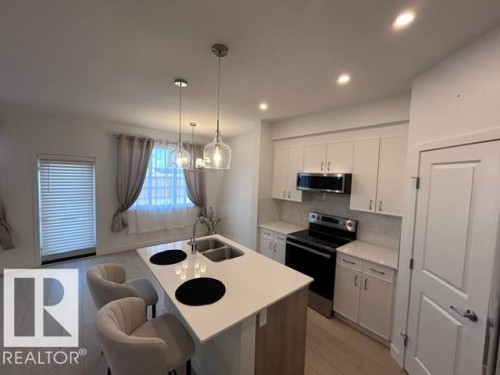 Kitchen featuring a central island with dual sinks, white cabinetry, integrated stainless steel appliances, and recessed lighting - 20936 16 Avenue Nw, Edmonton, AB - Indoor Photo Showing Kitchen With Double Sink