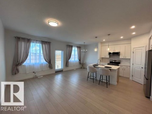 Open-concept living area featuring wood-finish flooring, recessed lighting, and a kitchen with white cabinetry, stainless steel appliances, and a central island with pendant lighting - 20936 16 Avenue Nw, Edmonton, AB - Indoor
