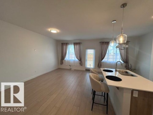 Open-concept living space featuring wood-finish flooring, a kitchen island with integrated sink, pendant lighting, and an exterior door - 20936 16 Avenue Nw, Edmonton, AB - Indoor
