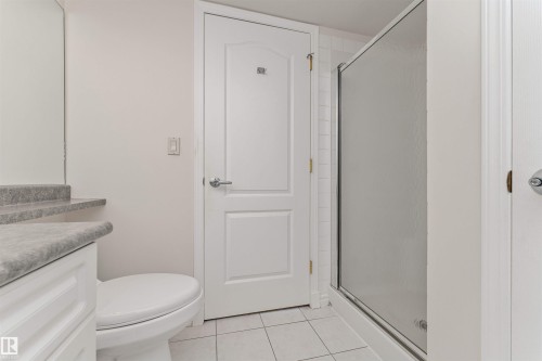 White vanity with a stone-finish countertop, white toilet, and enclosed shower with a translucent glass door - #1101 10909 103 Av Nw, Edmonton, AB - Indoor Photo Showing Bathroom