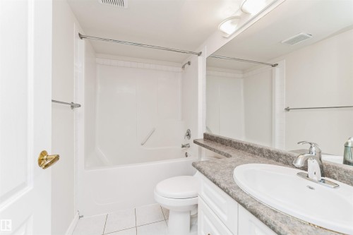 White bathroom featuring a bathtub with shower, white toilet, vanity with integrated sink, and a large mirror - #1101 10909 103 Av Nw, Edmonton, AB - Indoor Photo Showing Bathroom