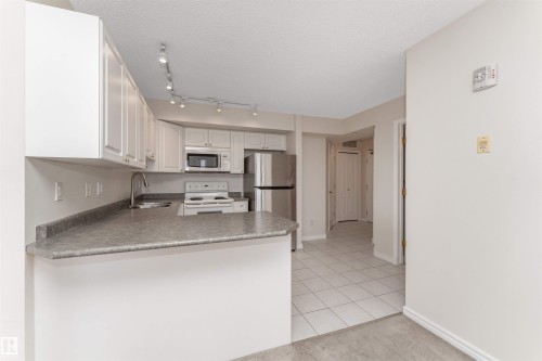 Kitchen featuring white cabinetry, track lighting, stainless steel appliances, a double basin sink, and a breakfast bar - #1101 10909 103 Av Nw, Edmonton, AB - Indoor Photo Showing Kitchen