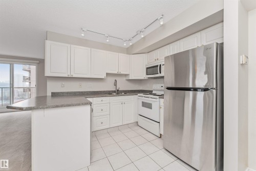 Kitchen featuring white cabinetry, gray countertops, stainless steel refrigerator, white range, and white tiled flooring - #1101 10909 103 Av Nw, Edmonton, AB - Indoor Photo Showing Kitchen With Double Sink
