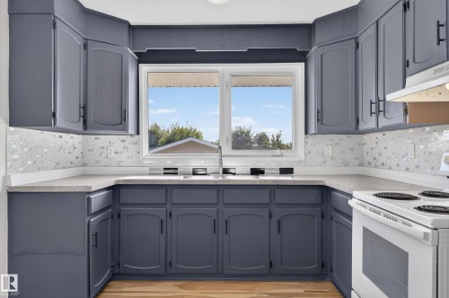 U-shaped kitchen featuring charcoal cabinetry, light-toned countertops, a multi-textured backsplash, and a double-basin sink - 13903 87 Street Nw, Edmonton, AB - Indoor Photo Showing Kitchen