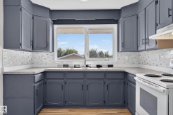 U-shaped kitchen featuring charcoal cabinetry, light-toned countertops, a multi-textured backsplash, and a double-basin sink - 