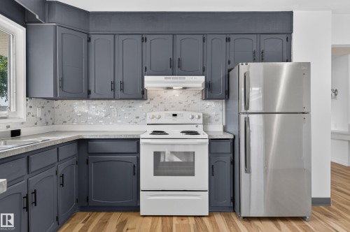 Kitchen featuring dark gray cabinetry, white countertops, mosaic tile backsplash, stainless steel refrigerator, and wood-finish flooring - 13903 87 Street Nw, Edmonton, AB - Indoor Photo Showing Kitchen