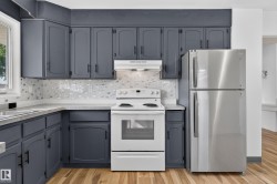 Kitchen featuring dark gray cabinetry, white countertops, mosaic tile backsplash, stainless steel refrigerator, and wood-finish flooring - 