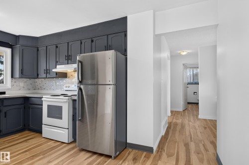 Kitchen featuring dark cabinetry with black hardware, white tile backsplash, white oven, and stainless steel refrigerator - 13903 87 Street Nw, Edmonton, AB - Indoor Photo Showing Kitchen