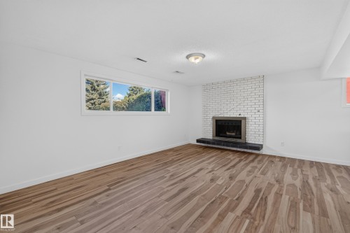 Expansive room featuring wood-finish flooring, a white brick fireplace, and a broad window - 13903 87 Street Nw, Edmonton, AB - Indoor Photo Showing Living Room With Fireplace