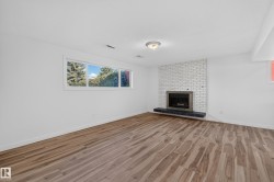 Expansive room featuring wood-finish flooring, a white brick fireplace, and a broad window - 